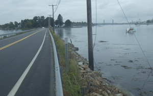 Photo shows roadway with water on either side and utility poles.