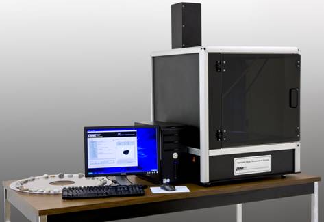 Figure 2. Photo. New Aggregate Imaging System equipment (AIMS2) (photo courtesy of Pine Instrument). The AIMS2 apparatus is shown on a narrow table. On the right is a black cube that appears to be about 30 inches in each dimension. The front has a label with the words “Aggregate Image Measurement System” and “Pine Instrument Company.” There is a square door on the front with a handle, and a chimney-like protrusion from the top rear of the box that is about one-third the height of the box. To the left of the box sits a computer tower, monitor displaying text and graphic, keyboard, and mouse. Behind them, lying flat on the table, is a flat translucent white disk, about 2 ft in diameter, with a large round hole in the center. About 1 in. inside the outer edge of the disk, a recessed circle contains pieces of aggregate, closely spaced, in a single row around the disk. 