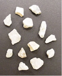 Figure 2.11. Photo. Light 4.75 mm (ASTM #4 sieve) Aggregates used in Experiment 5. Several pieces of light-colored aggregate are shown on a dark-colored background.