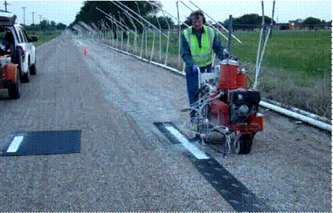This picture shows a crew member behind the EZ Liner pavement marking application cart in the process of calibrating the bead drop rate by applying a certain setting on the cart on a piece of sample pavement marking paint.