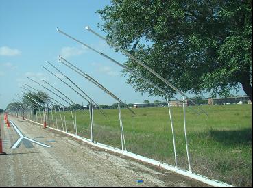This image shows a south-southwest bound view of the rain range taken from eye height at the north end of the rain tunnel. The main pipe is positioned along the west edge of the roadway, where smaller piper are vertically raised and extended over the roadway. The terminal point of each pipe at the highest point is a nozzle facing upward.