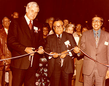 Cutting a Ribbon: Federal Highway Administrator Norbert T. Tiemann (left) and The Reverend Jerry Moore (right), a D.C. City Councilman, hold the ribbon as Secretary of Transportation William T. Coleman, Jr. open the Bicentennial Exhibit 'Highways of History' on March 31, 1976, in the Old Pension Building (now the National Building Museum).