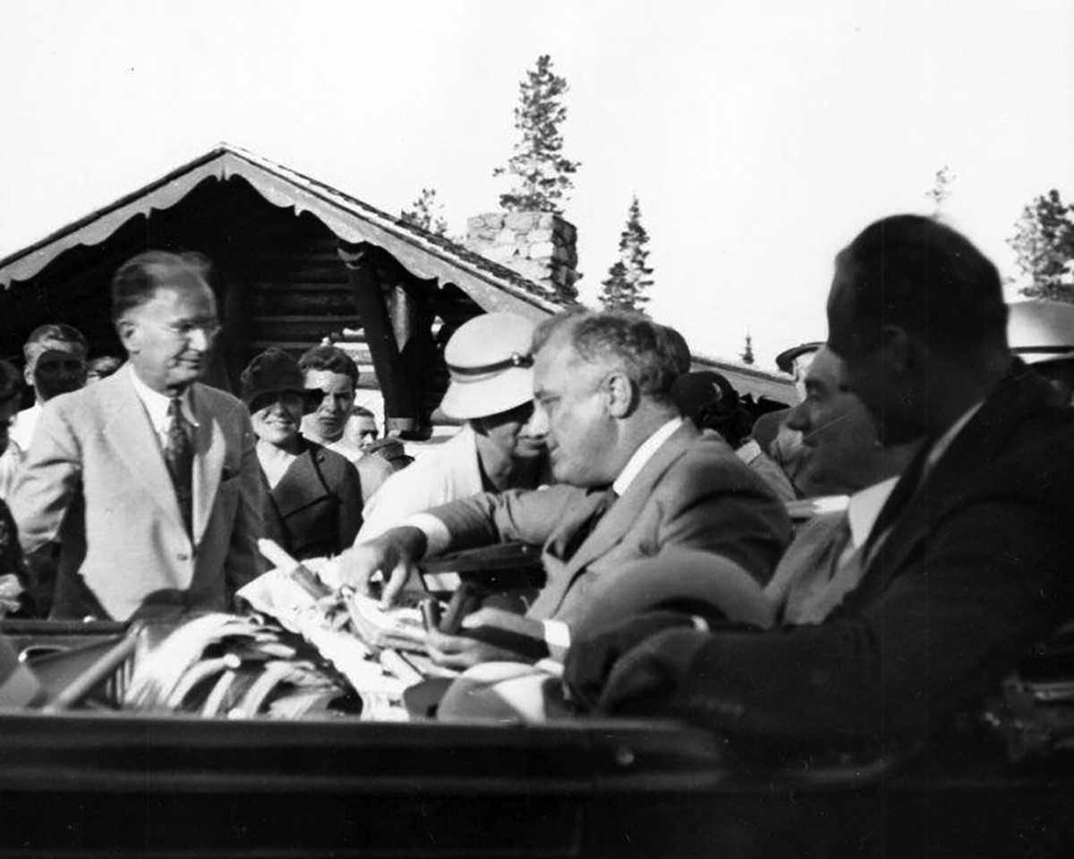 On August 5, 1934, President Franklin D. Roosevelt and First Lady Eleanor Roosevelt talk while Senator Burton K. Wheeler of Montana looks on at Two Medicine. The president is holding a pipe presented to him by the Blackfoot Indians, while Wheeler stands alongside car.  (Glacier Park National Archives)