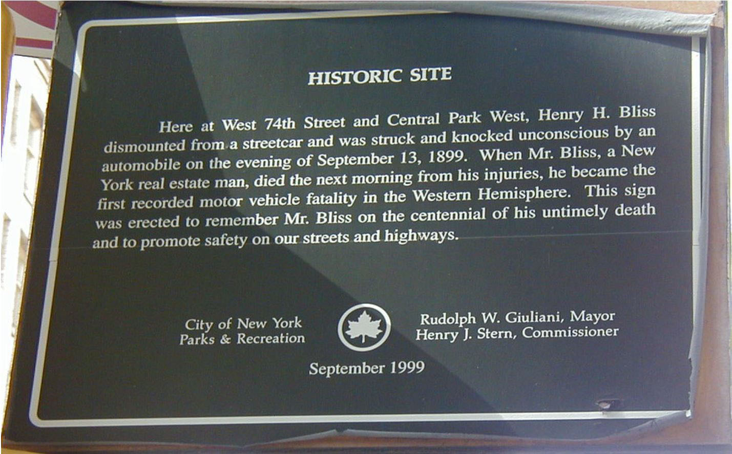 Photograph of the Hostoric plaque. It reads: Here at West 74th Street and Central Park West, Henry H. Bliss dismounted from a streetcar and was struck and knocked unconscious by an automobile on the evening of September 13, 1899. When Mr. Bliss, a New York real estate man, died the next morning from his injuries, he became the first recorded motor vehicle fatality in the Western Hemisphere. This sign was erected to remember Mr. Bliss on the centennial of his untimely death and to promote safety on our streets and highways.