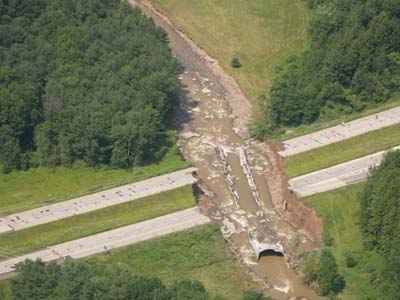 Photograph. Water, mud, and debris, due to a failed culvert, make a dual highway and its median impassable in both directions.