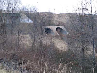Photograph. A pair of large concrete culverts cross under a highway.