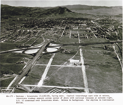 Montana - Interstate 15-4(6)182, facing west.  Capitol interchange east side of Helena, with Interstate roadway appearing across center of photo with railroad overpass at extreme right.  U.S. 12 crossroad over Interstate shown.  Helena in background.  Far skyline is Continental Divide.