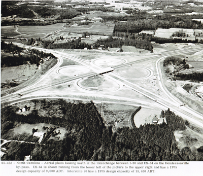 North Carolina - Aerial photo looking north at the interchange between I-26 and U.S. 64 on the Hendersonville by-pass. U.S. 64 is shown running from the lower left of the picture to the upper right and has a 1975 design capacity of 9,000 ADT.  Interstate 26 has a 1975 design capacity of 15,400 ADT.