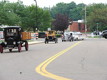 Vintage cars drive down a street in this modern photograph.