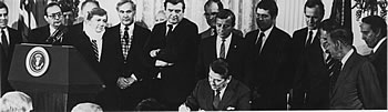 President Reagan signs bill while others look on.