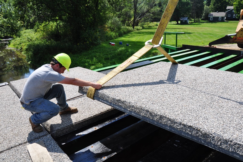 The photo depicts how prefabricated deck panels were attached in a project by bolting from below with no penetrations on top. The panels measured 7.5 feet x 11 feet and weighed 17 pounds per square foot.