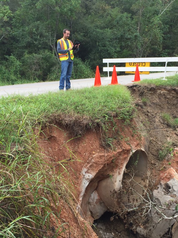 The photo shows damage to a concrete headwall and culvert. A person is shown inputting assessment data in a tablet.