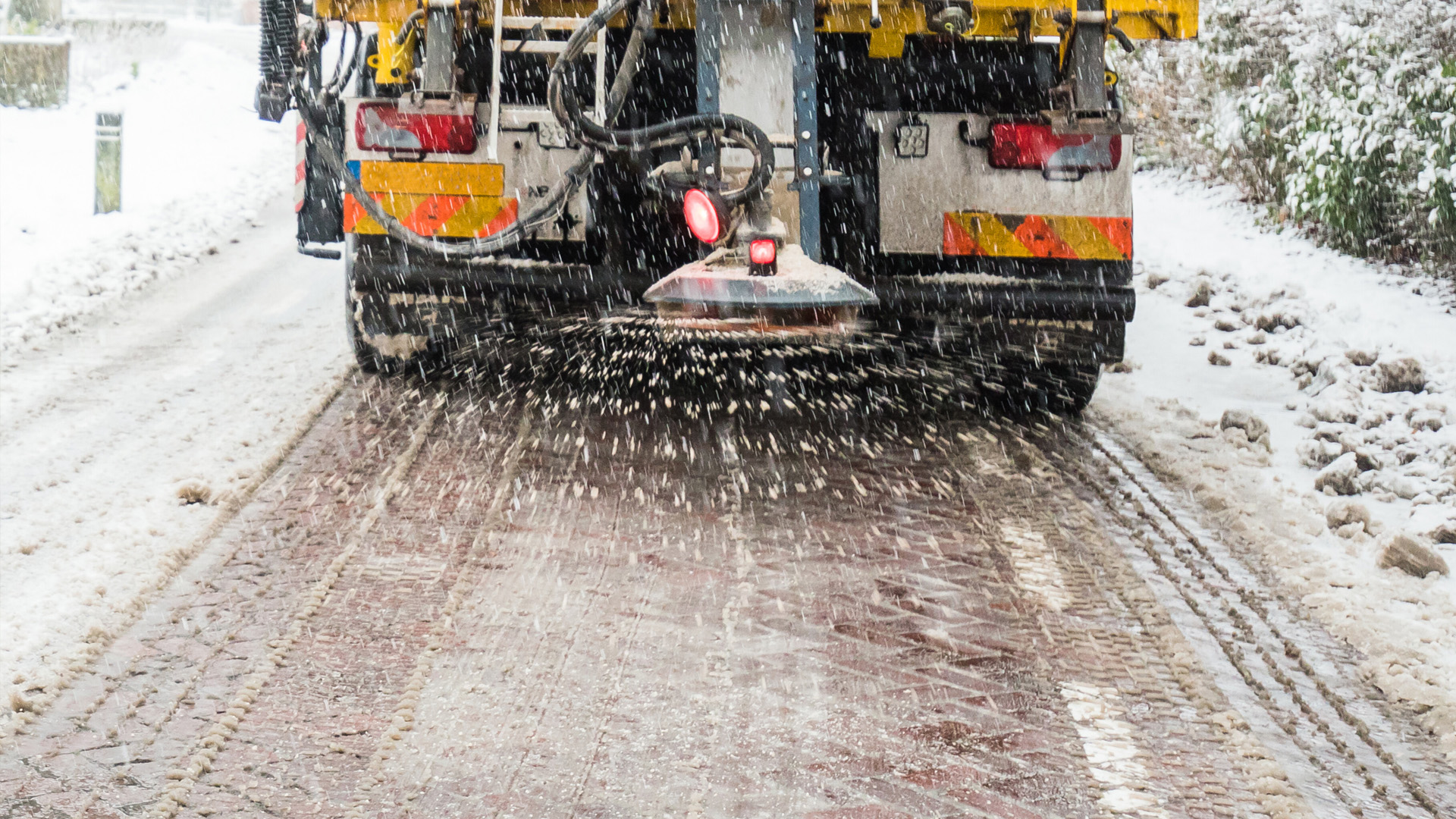 The rear end of a salt truck dispensing salt on a snowy road.