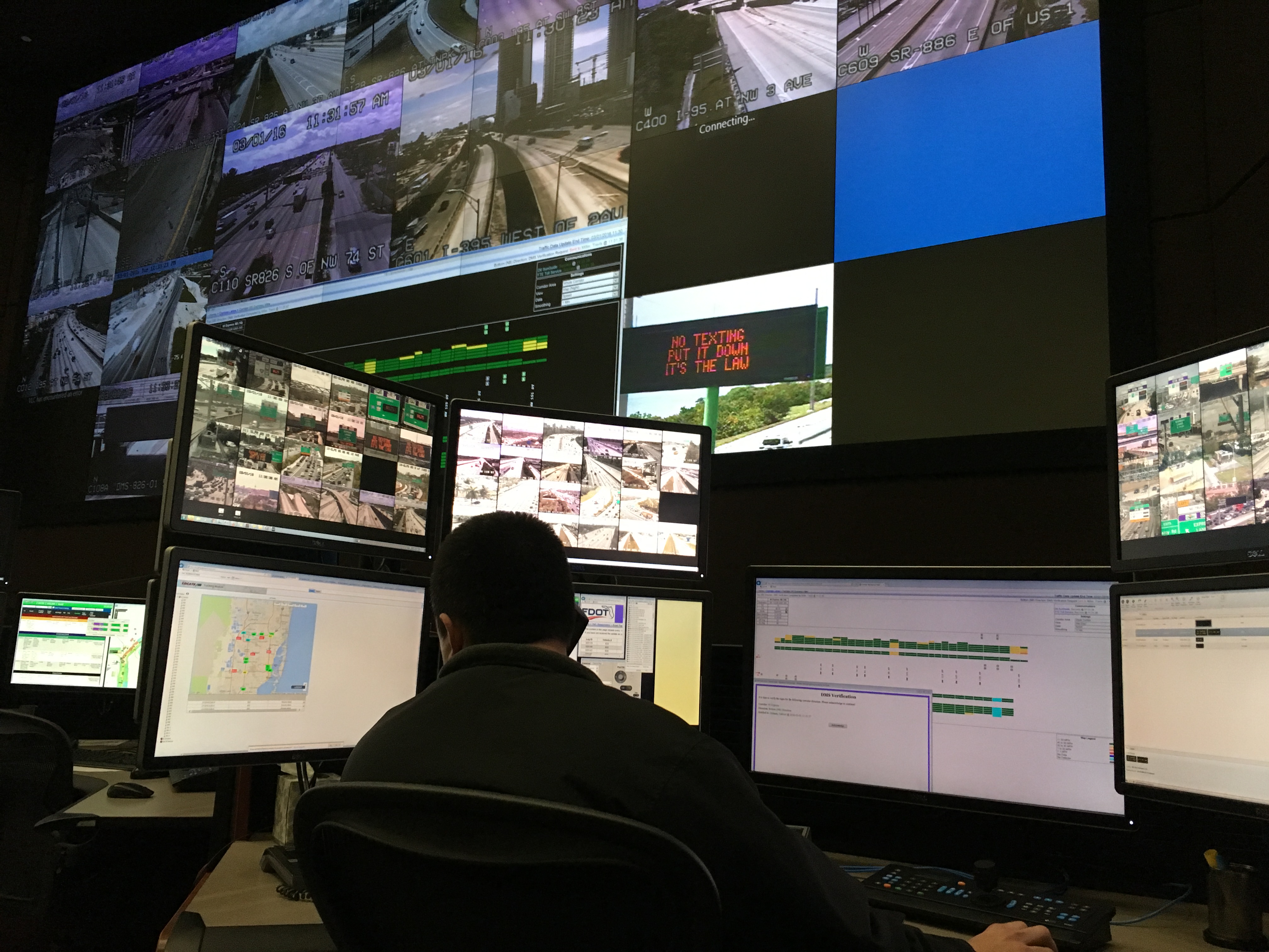 A man sitting at an array of monitors in a traffic control center.