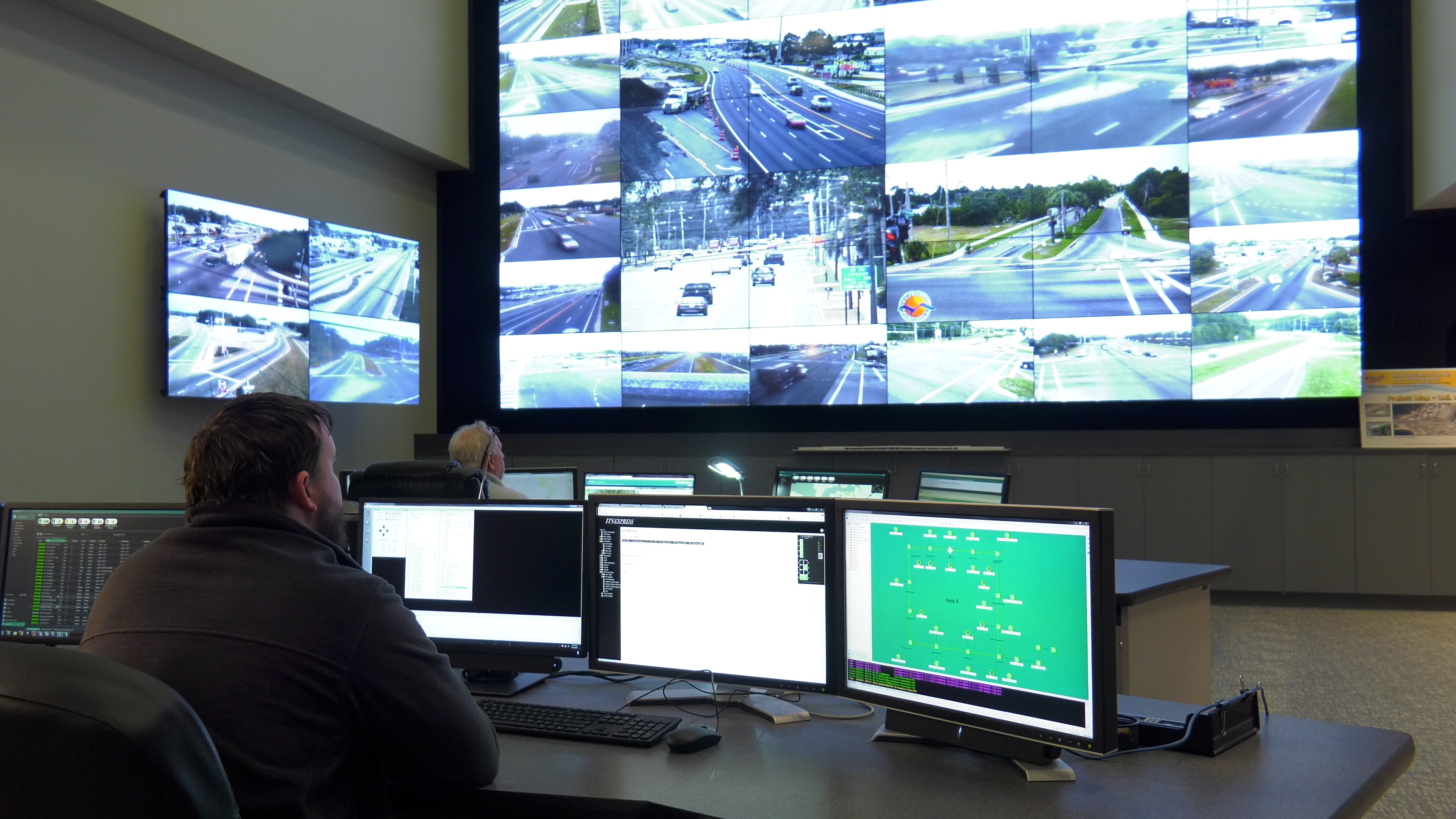 A man sitting at an array of monitors in a traffic control center.