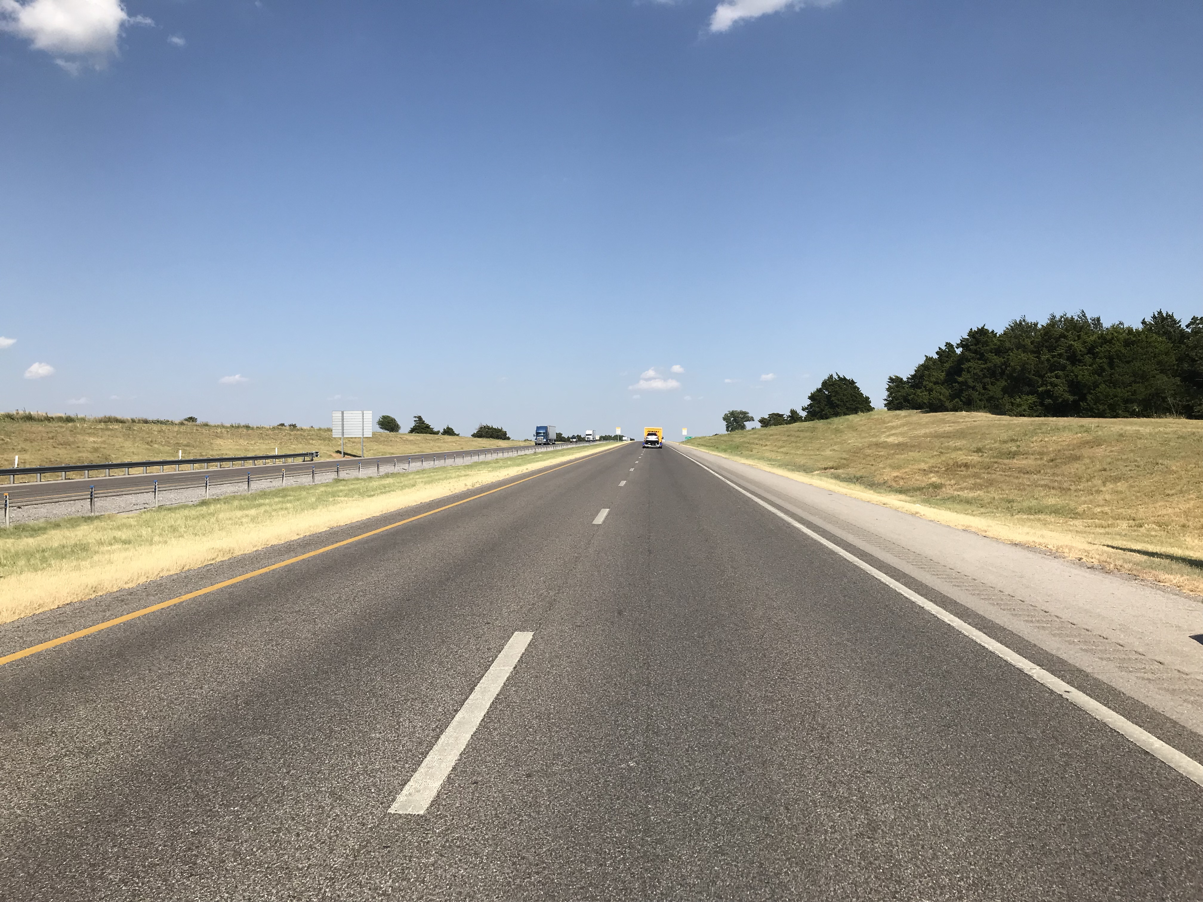 Four lane asphalt highway with traffic in the distance and blue skies.