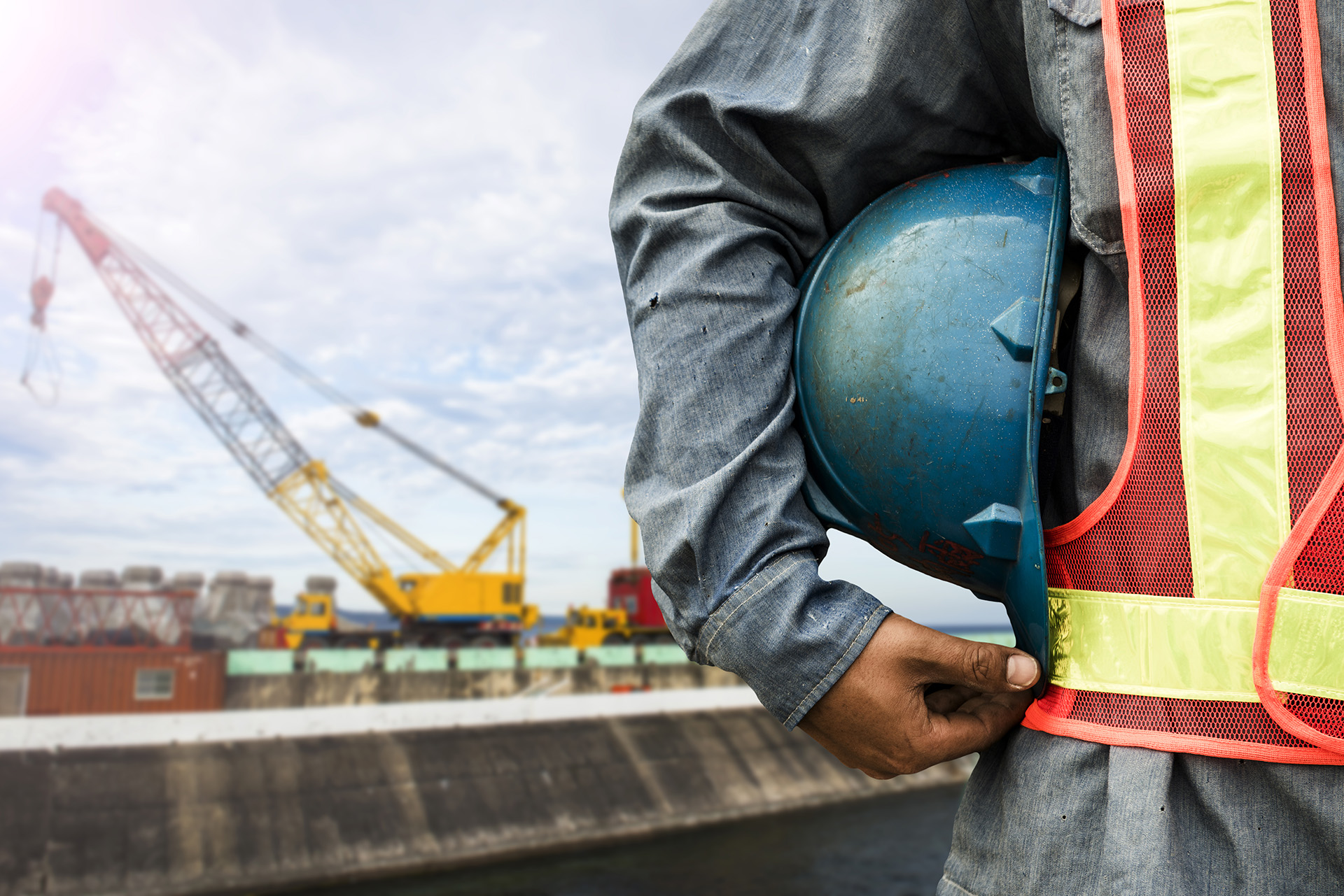 Construction worker wearing a safety vest holding a hard hat under his arm.