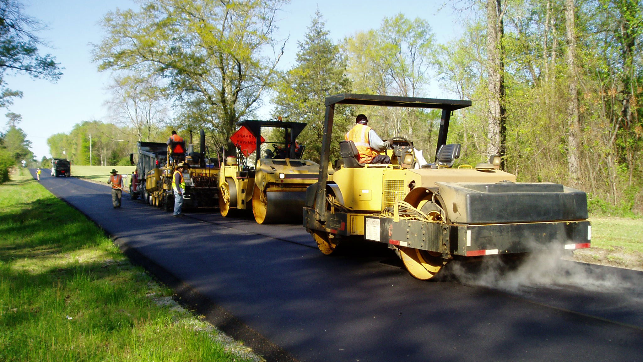 Image of multiple steam rollers packing a two-lane rural asphalt road.