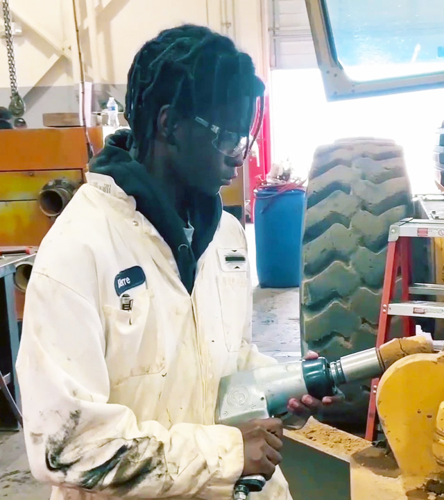 Video of young man in coveralls removing a nut from a road grader.