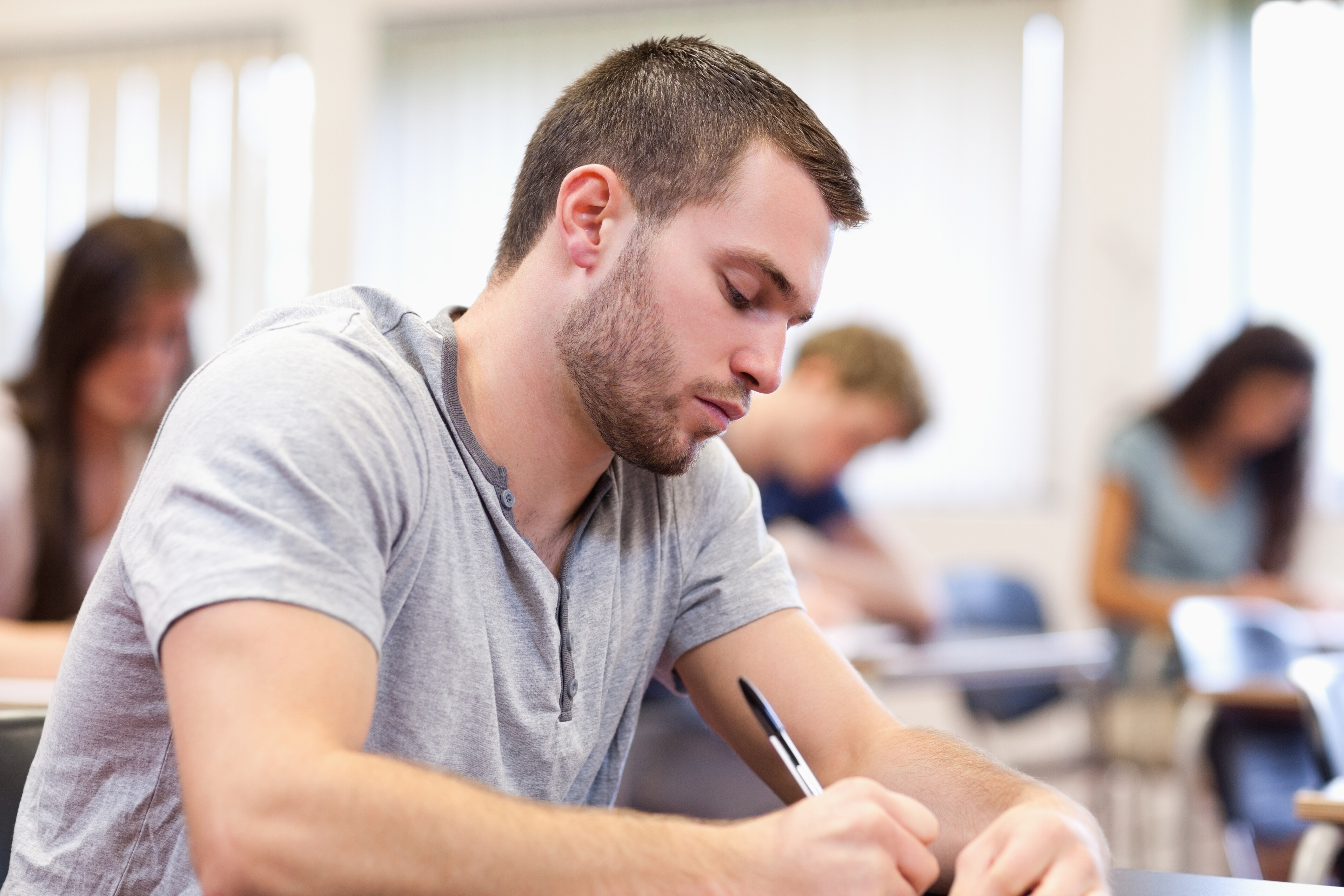 A man sitting in a classroom at a desk writing.