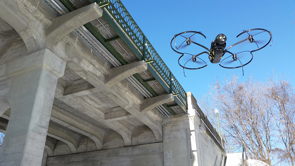 A drone flies next to a bridge.