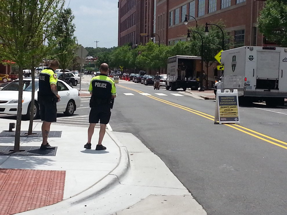 Two police officers stand on a curb and monitor pedestrians' use of the crosswalk.