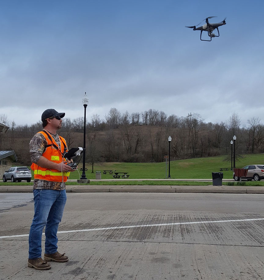 UAS operator, left, stands in a parking lot as his drone, visible at right, takes off.”
