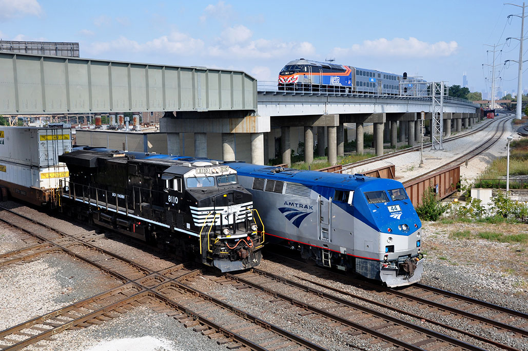 Multiple trains cross a railway junction, including one on a rail flyover.