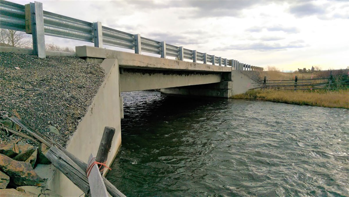 Low-angle photograph of small bridge extending over a waterway in rural area.