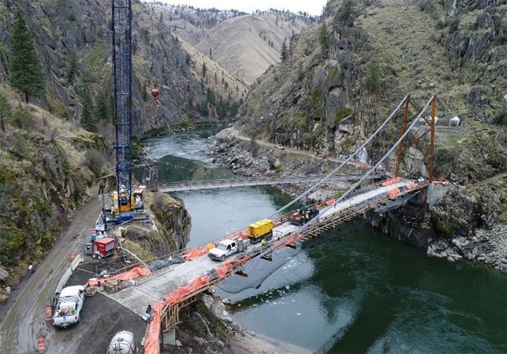 A suspension bridge under-construction extends across a river.