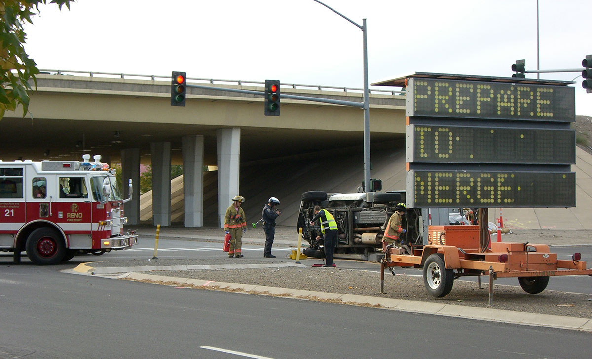First responders gathered at a traffic incident. Digital signage, at right, tells drivers to "prepare to merge." Several first responders and a fire truck are positioned at left.