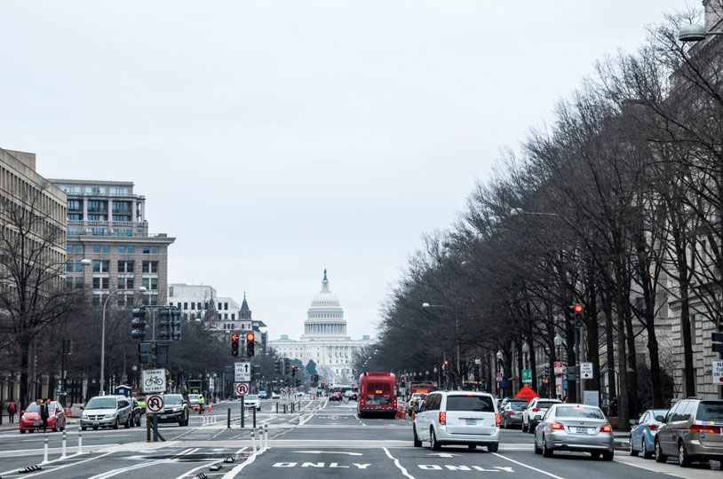 View of Washington D.C. street with U.S. Capitol in background. A pedestrian crosses at a signal.