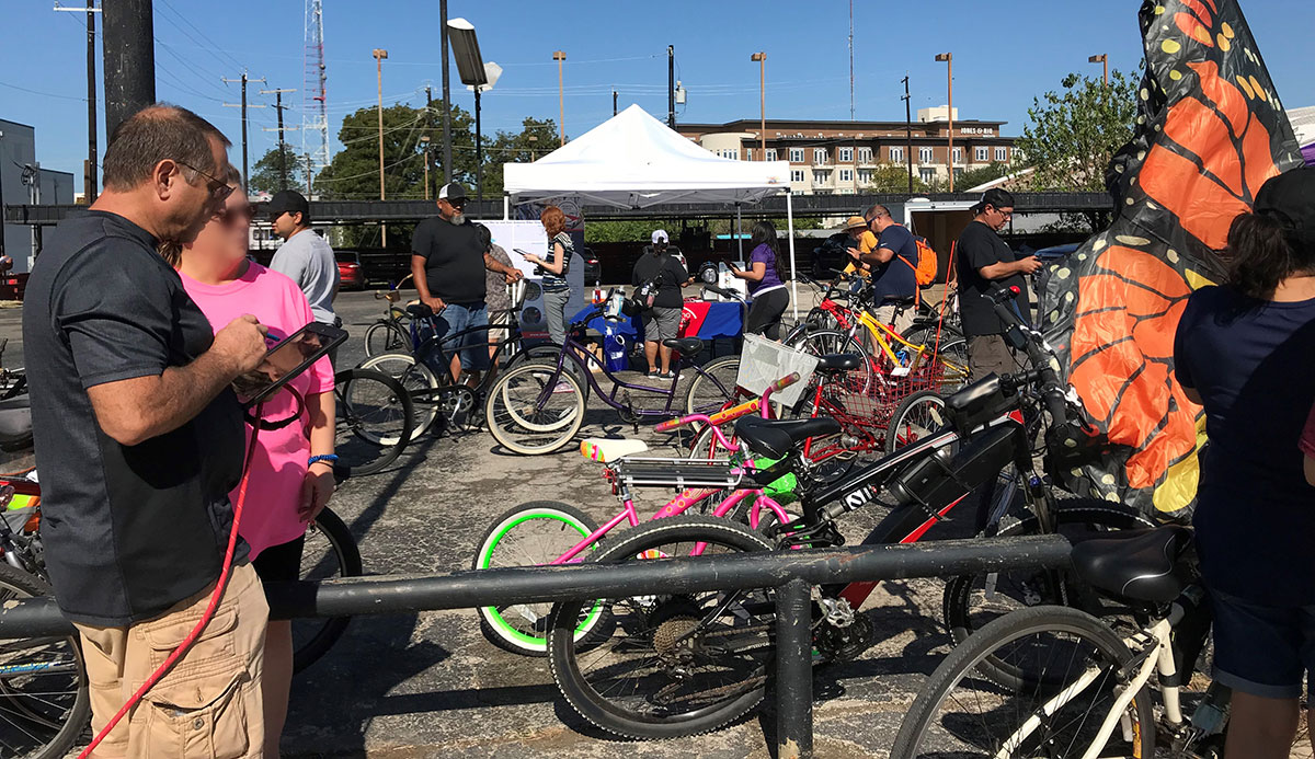 Man holding tablet speaking to a woman at an outdoor gathering near a large number of parked bicycles.