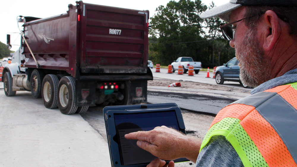 Worker with tablet collects e-Ticket information from dump truck delivering material to a site.