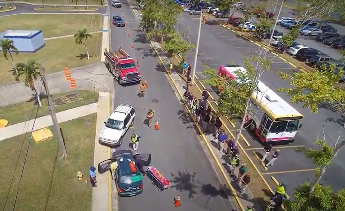 Aerial photo of training scene, including vehicles, emergency responder vehicles, safety equipment, traffic cones, and barrels.