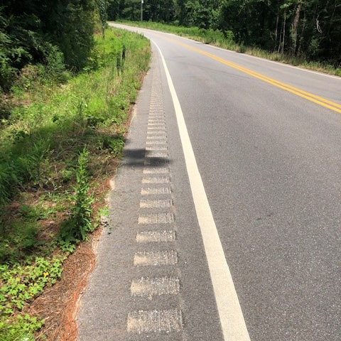 Closeup of roadway showing a widened shoulder and rumble strips.