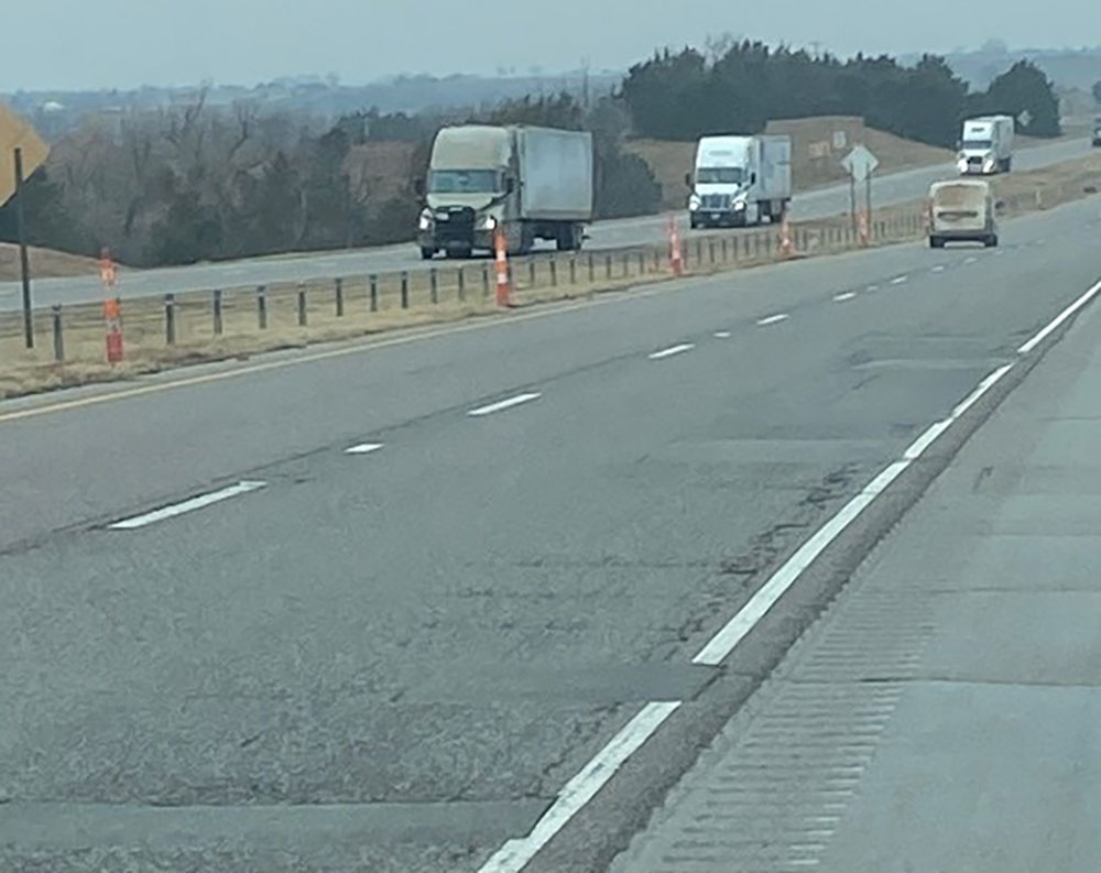 A 4-lane, divided interstate road. Trucks are approaching in left lanes, another vehicle is heading away from camera.