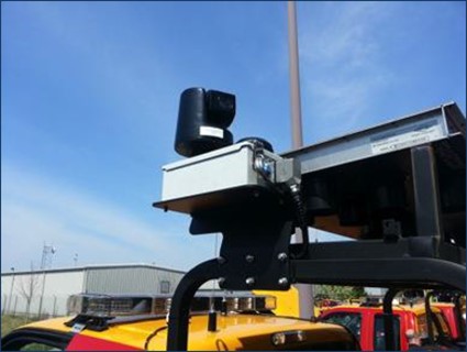A camera mounted in a housing on top of a bar, coming off of the back of a truck.