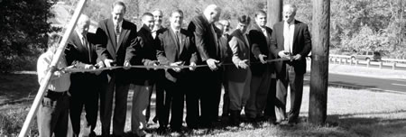 Photograph of 12 area officials and representatives of the Virginia DOT and FHWA cutting a ribbon at the Buckland Bridge dedication.