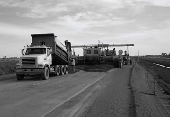 Photograph showing a construction paver pouring concrete over asphalt.