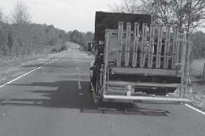 Photograph showing the rear of an automated pavement marker placement system. It fits on a truck and eliminates the need for a worker riding under the truck to apply markers by hand. Photo Credit: Stay Alert Safety Services