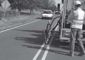 Photograph of the rear of an automated pavement marker placement system and FHWA's Carl Andersen observed the operation during a field test. Photo Credit: Stay Alert Safety Services