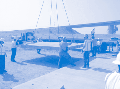 Workers positioning prefabricated slab into position with crane.