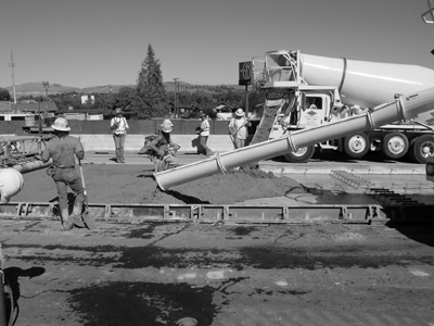 Road workers laying out concrete over framed roadway.