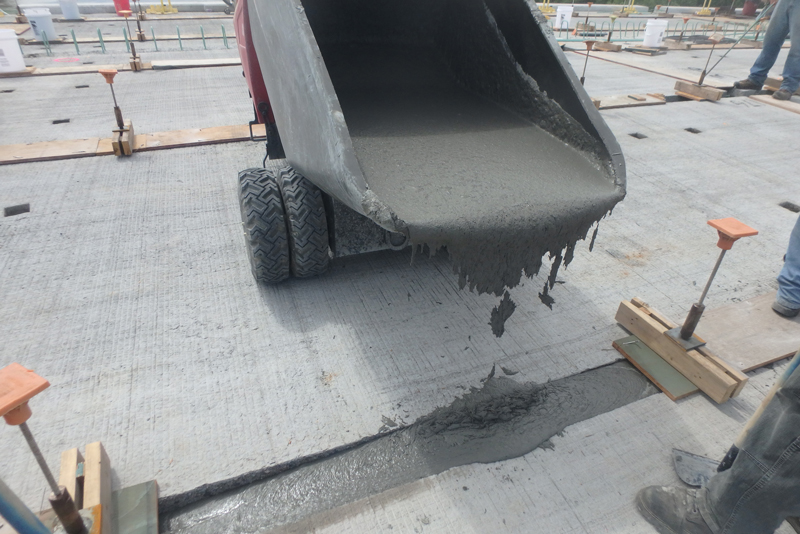 Photo of Ultra High Performance Concrete being poured from a wheelbarrow into a gap between bridge deck panels of the Franklin Avenue Bridge in July 2016