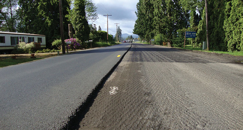 Photo of a road with one side grated and the other with recent pavement preservation treatment.