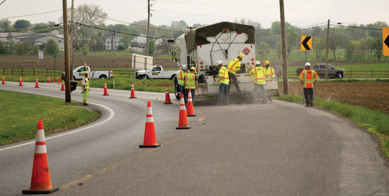 Workers and truck applying high-friction surface treatment on a roadway curve.