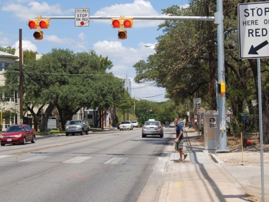 Photo of pedestrian in a crosswalk with a pedestrian hybrid beacon overhead.