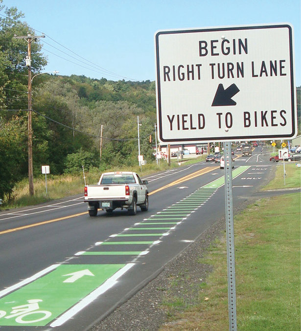 Photo of road diet showing vehicle and green-painted bike lanes, with roadside sign reading “begin right turn lane—yield to bikes.”