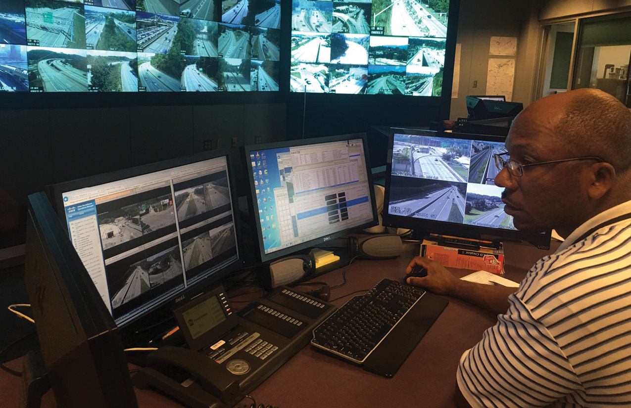 Photo of man monitoring road and traffic information on a set of computer screens.